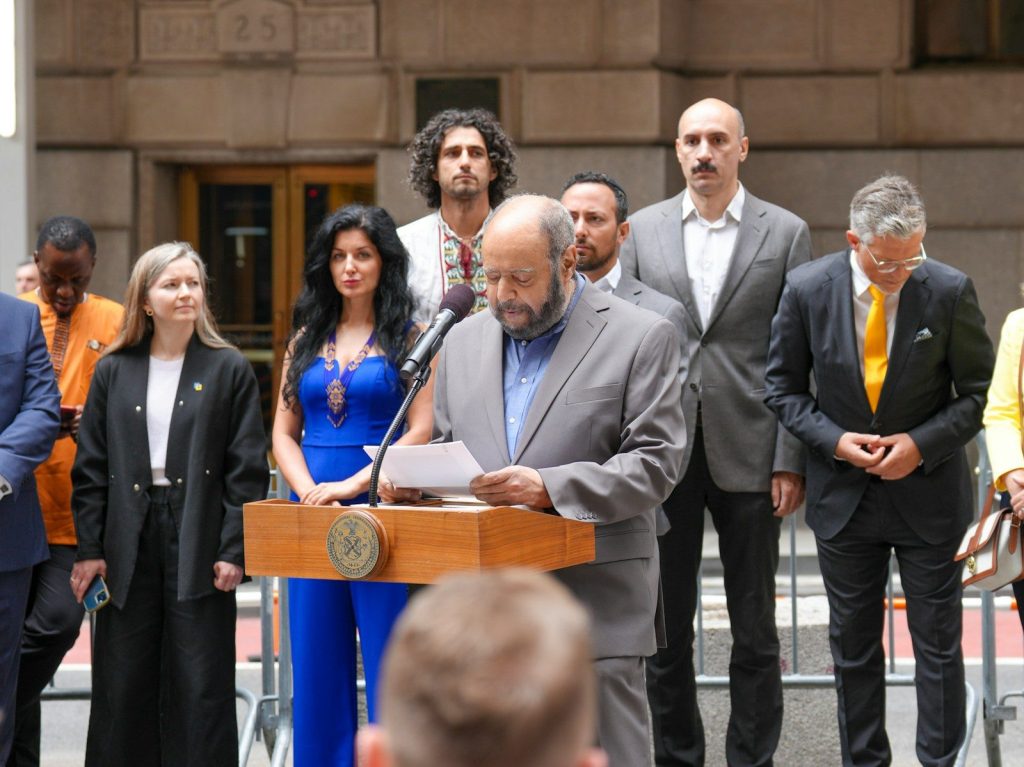 Man speaks at podium with diverse group behind him